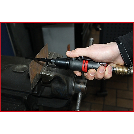 Hand hält eine Stichsäge, schneidet Metallplatte. Die Säge ist schwarz mit roten Akzenten. Die Metallplatte wird in einem Schraubstock gehalten.